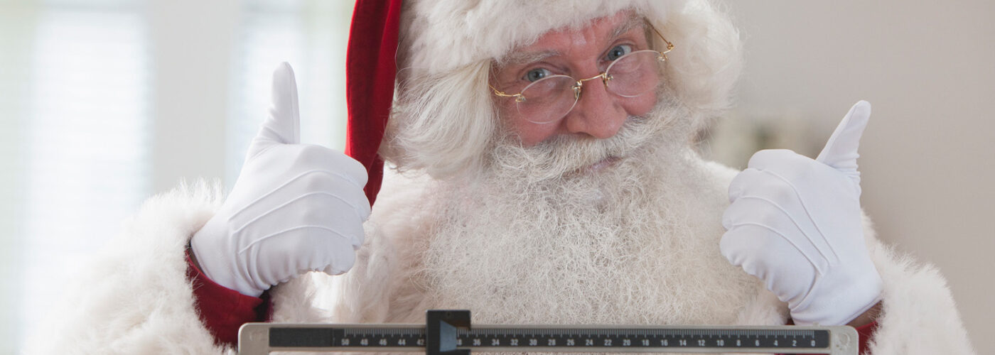 Santa Claus standing on a scale holding two thumbs up